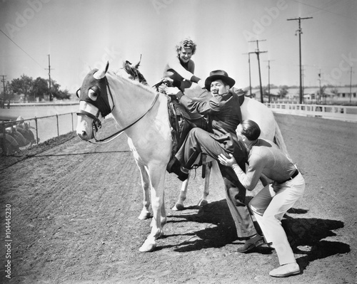 Young couple trying to help a man get onto his horse 