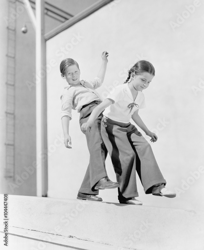 Boy and girl trying to balance on a ledge 
