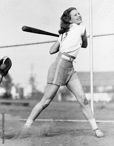 Canvas Print Young woman swinging a baseball bat in a baseball field