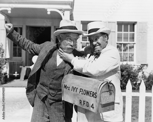 Tablou pe pânză Two mature men fighting near a mail box in front of a house