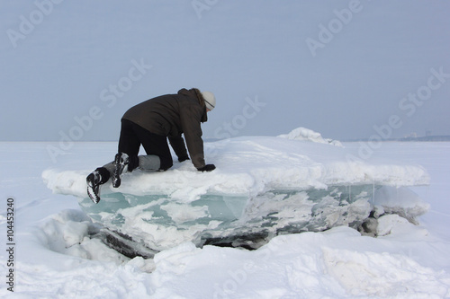 The man in a gray cap moving along  the ice block on the river