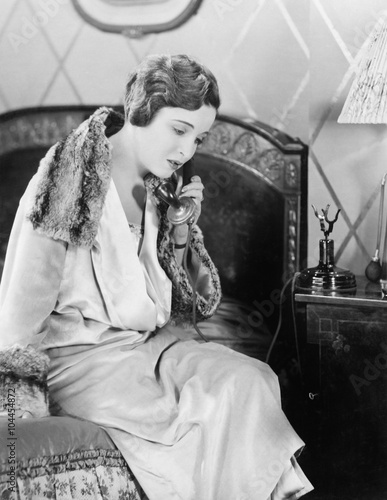 Young woman sitting on her bed in the bed room, speaking on the telephone 