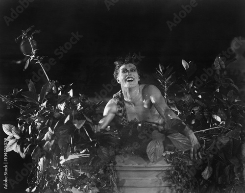 Portrait of a young man sitting on a wall with lowers and plants and smiling 
