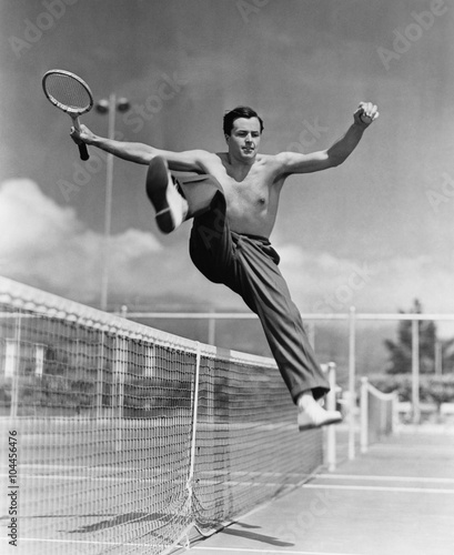 Male tennis player jumping over net  © everettovrk