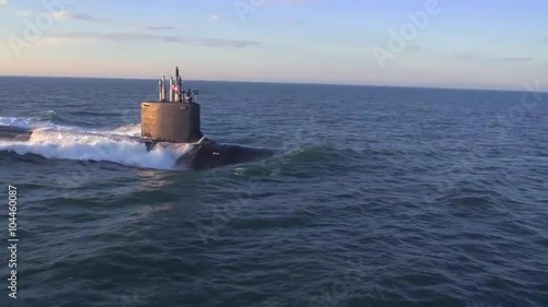 Excellent aerials over a submarine at sea with dolphins jumping across bow. photo