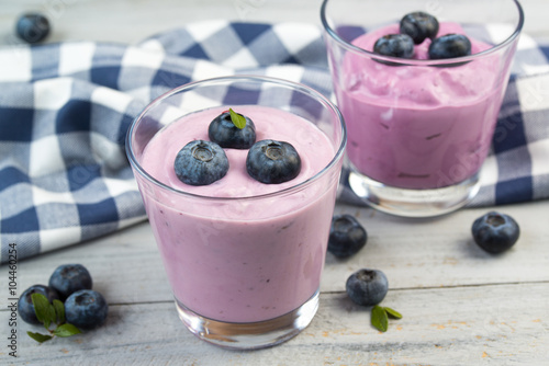Two glasses with blueberry yogurt and fresh berries on wooden table