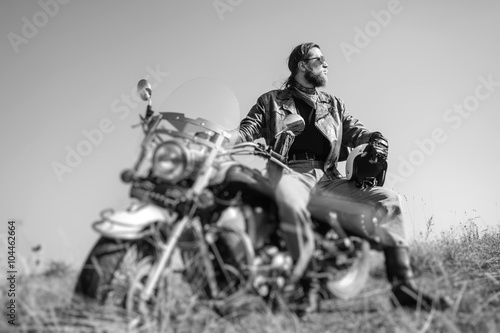 Fotografie Portrait of a young man with beard sitting on his cruiser motorcycle and looking to the sun