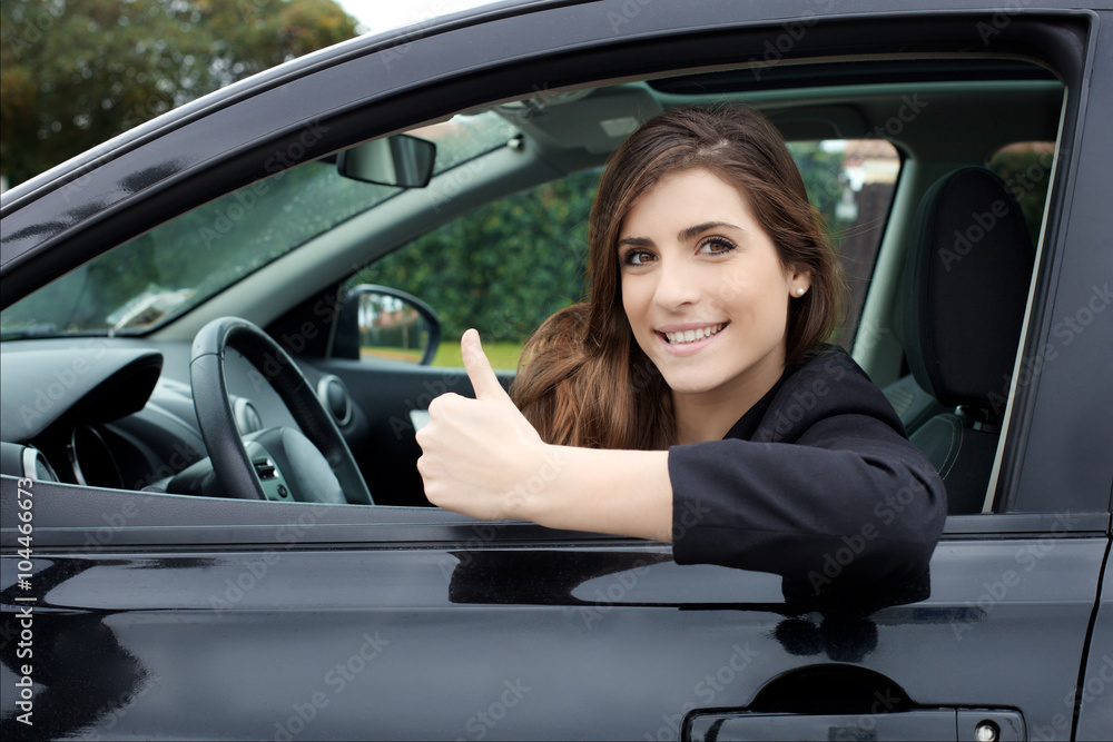 Happy young woman in new car looking camera smiling thumb up