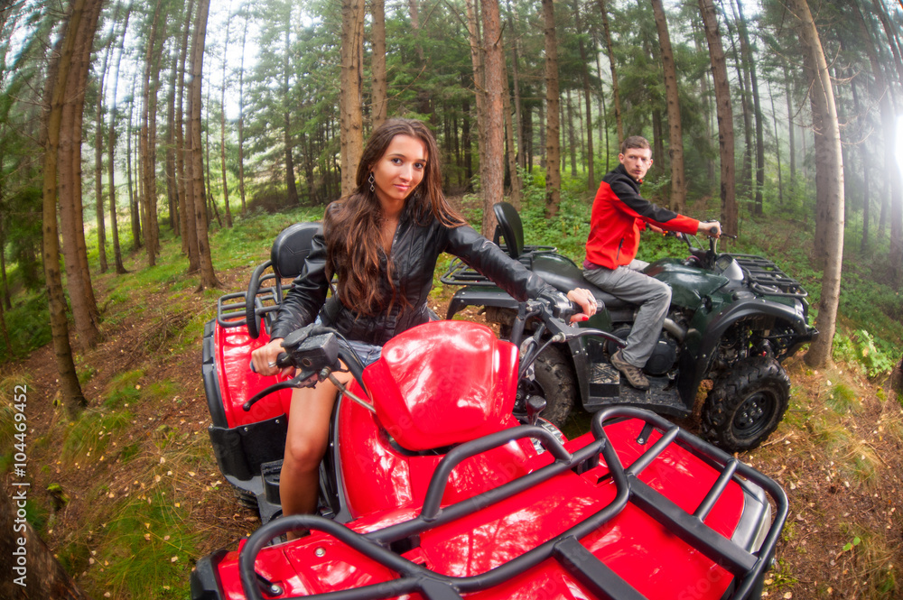 Happy beautiful couple driving four-wheelers ATV. Lady is looking at the camera