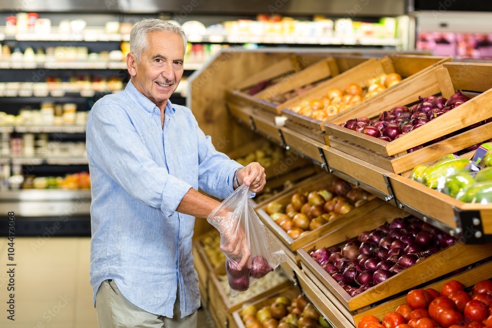 Smiling senior man buying red onions at the grocery shop