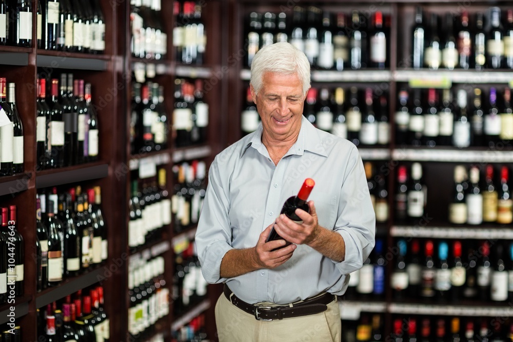 Smiling senior man choosing wine at the supermarket