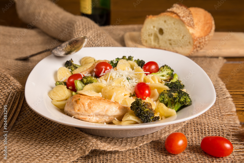 Authentic Italian meal with homemade orecchiette pasta, chicken, broccoli, tomatoes. Loaf of Italian bread and bottle of wine in the background Authentic Italian meal with homemade orecchiette pasta, chicken, broccoli, tomatoes. Loaf of Italian bread and bottle of wine in the background