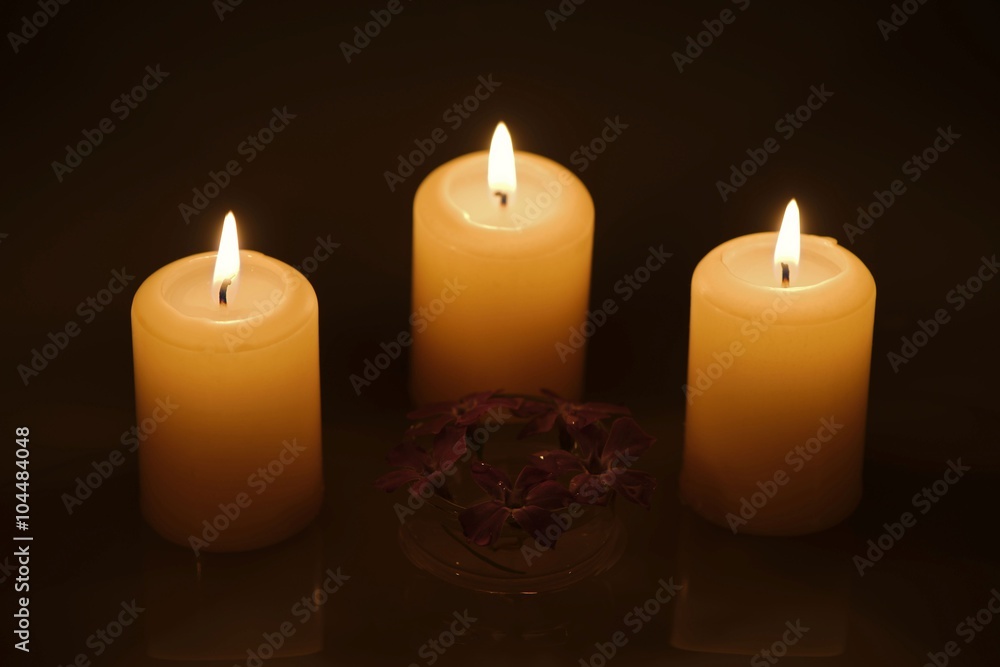 Three burning candles with water reflection and a glass bowl of tiny purple flowers Three burning candles with water reflection and a glass bowl of tiny purple flowers