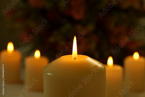 Line of burning candles with a big candle in the foreground against blurred flower background