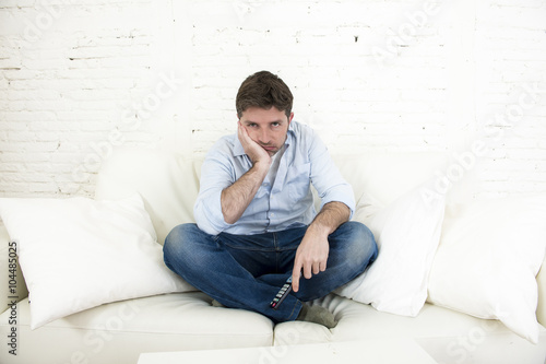 bored man watching television sitting on sofa holding remote control tired not having fun
