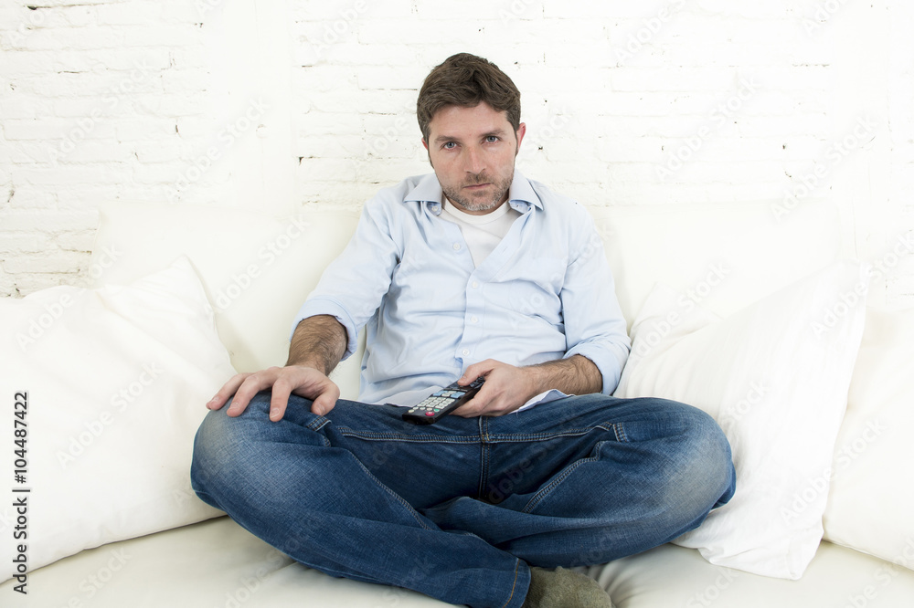 man watching television at home living room sofa with remote control looking very interested