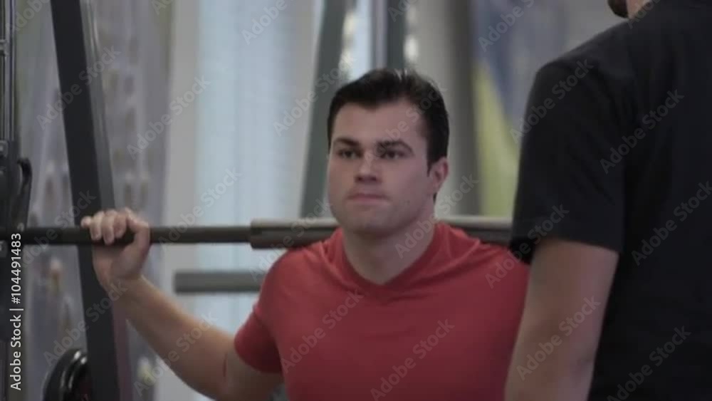 Tight shot of a man doing squat lifts while friend watches. Tight shot of a man doing squat lifts while friend watches.