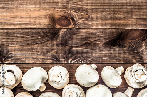 Whole mushrooms champignons on rustic wooden background.