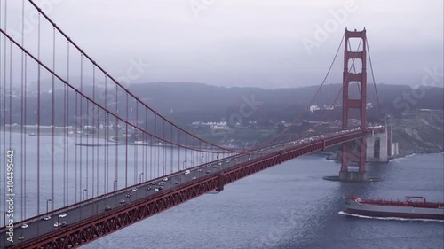 Medium tight static shot of the Golden Gate Bridge as a shipping barge goes under.