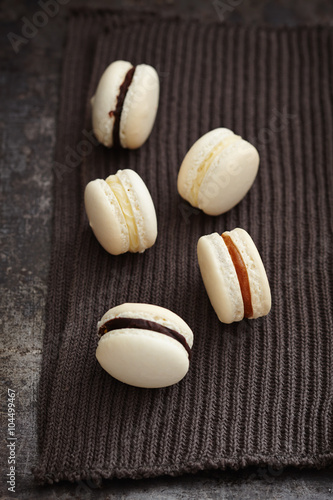 White macarons with caramel and chocolate filling on dark background