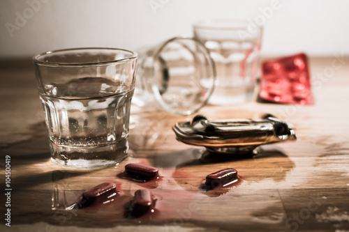 Mini car crash. Vodka shot, meting pills and overturned toy car on a table - metaphor of drunk driving. 