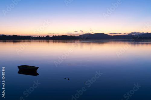 Small boat afloat on calm bay during brilliant sunrise.