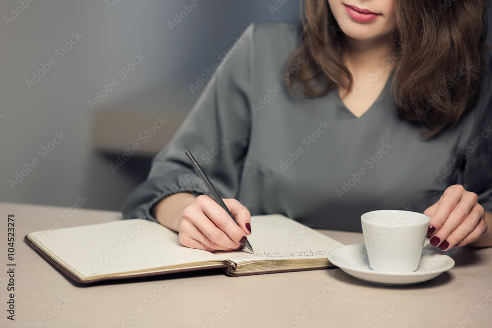 young adult female has coffee break in cafe and writing notes in diary or notepad; young adult female has coffee break in cafe and writing notes in diary or notepad;