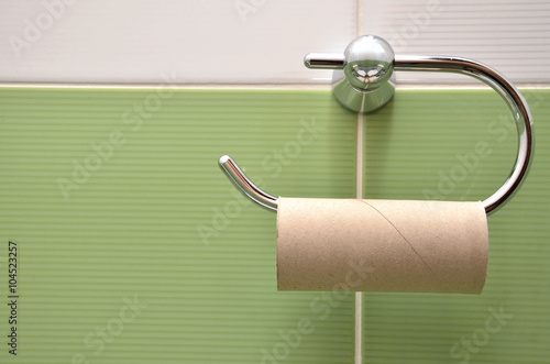 Empty roll on toilet paper holder with white and green tiles in background