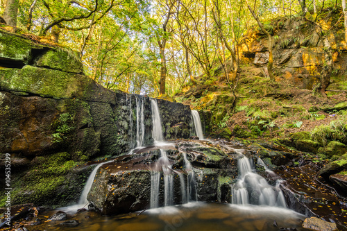 Peaceful trickling waterfall in a remote woodland forest on a summer afternoon with early Autumnal colours.