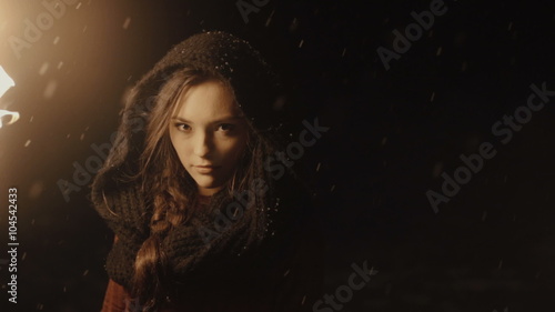Portrait of a young mystic woman in the dark forest holding a torch. Young woman over dark night background. Falling snow. Slow motion. photo