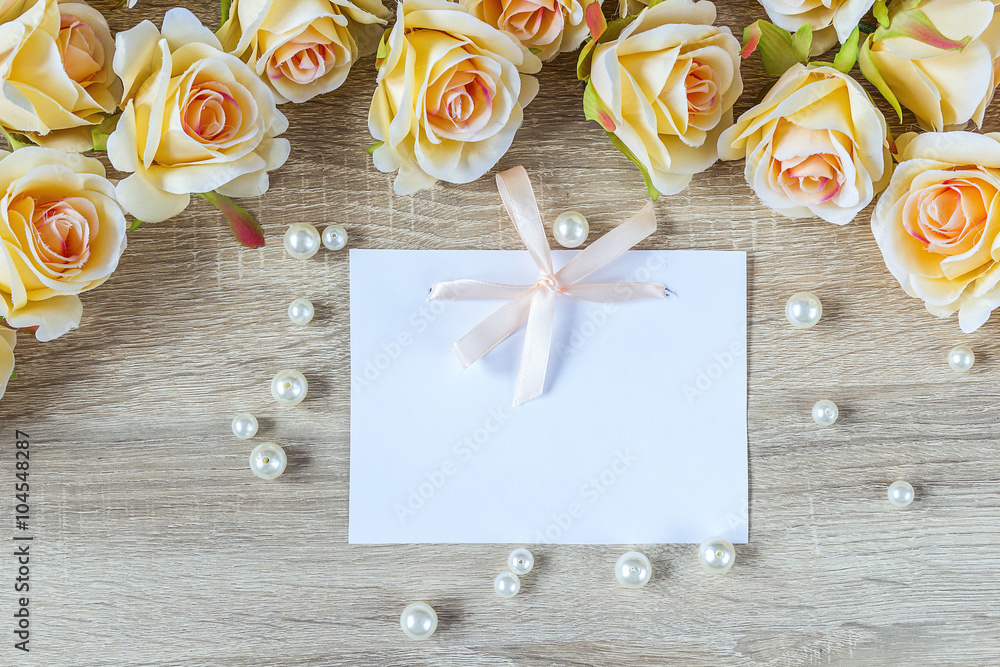 White blank card with a pink ribbon, peach roses and pearl on a