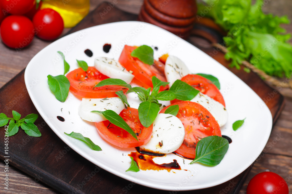 Caprese salad. Italian cuisine. Mediterranean cuisine. Tomatoes, mozzarella, basil leaves and olive oil on wooden table. 