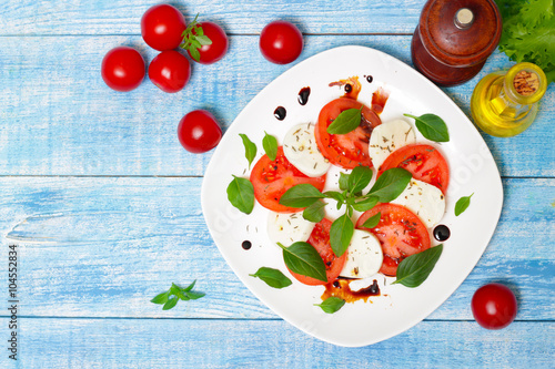 Caprese salad. Italian cuisine. Mediterranean cuisine. Tomatoes, mozzarella, basil leaves and olive oil on wooden table. 