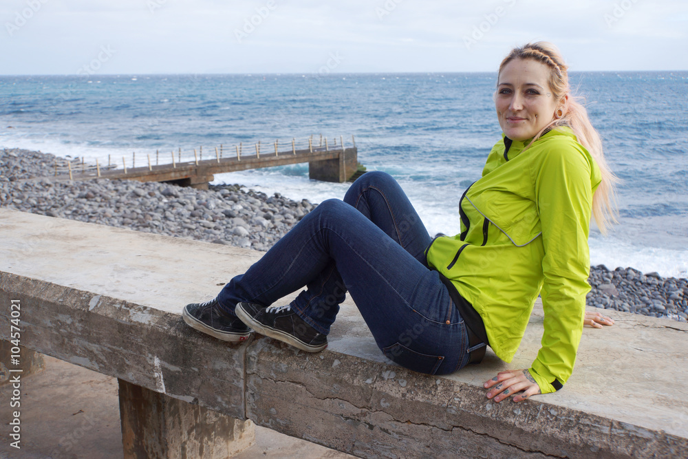 junge Frau sitzt auf Mauer an Uferpromenade