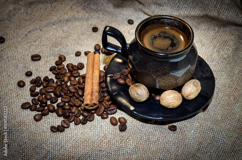 Coffee cup and coffee beans, nutmegs and cinnamon sticks on a sack background
