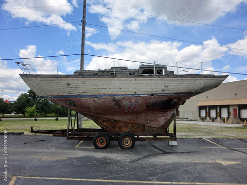 Old weathered vintage junk wooden sailboat in parking lot - landscape color photo