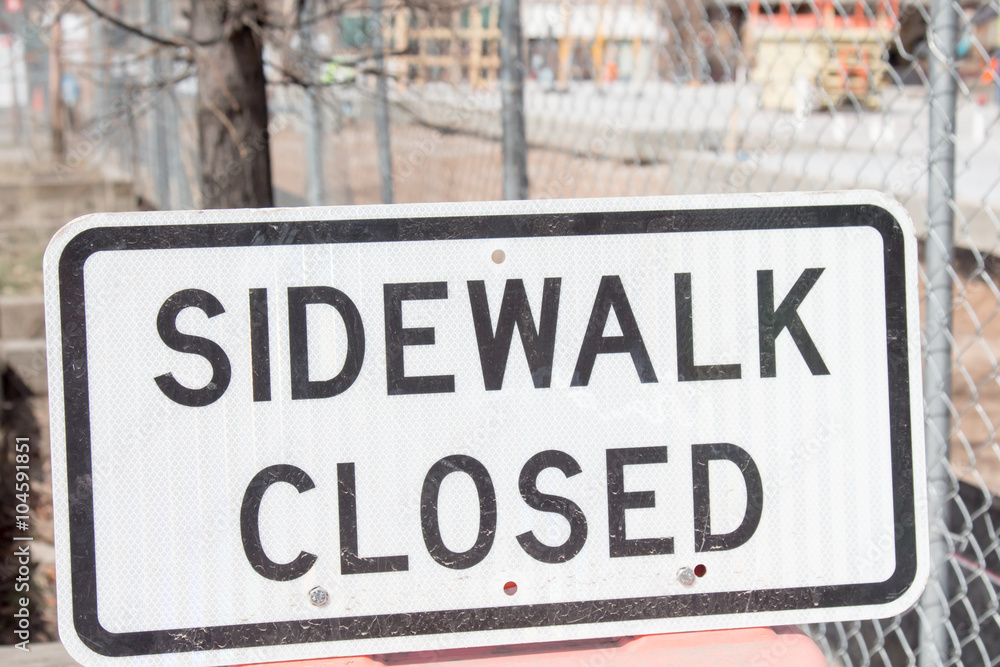 Sidewalk closed sign in front of a fence and construction zone Sidewalk closed sign in front of a fence and construction zone