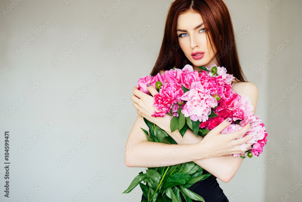 Long hair. Beautiful sexy girl with pink peony flowers. On a white background. With make-up, hair and manicure. Refined figure. Black swimsuit. Spring