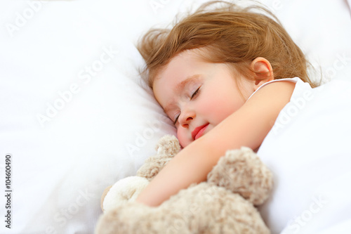 child little girl sleeps in the bed with teddy bear