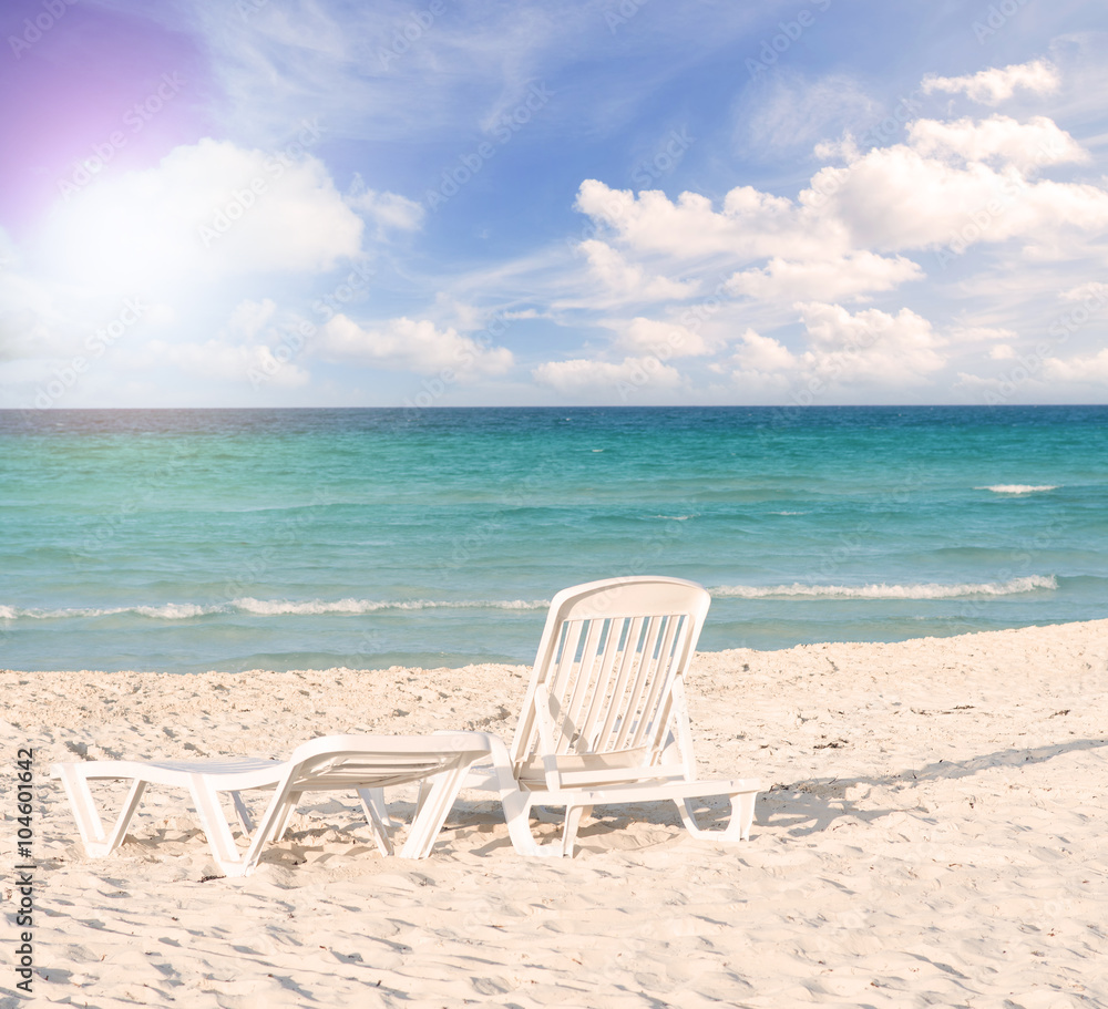 White plastic chairs on white sand beach with sun flare effect