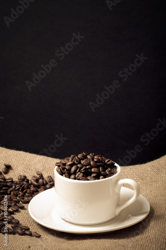 Cup, saucer and coffee beans on a burlap background. Toned
