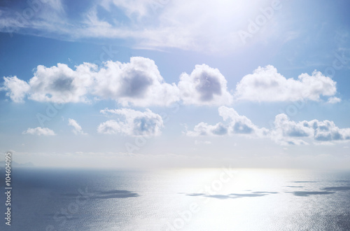 Beautiful small cumulus clouds with reflection on sea / ocean water surface with horizon and blue sky, during sunny day.