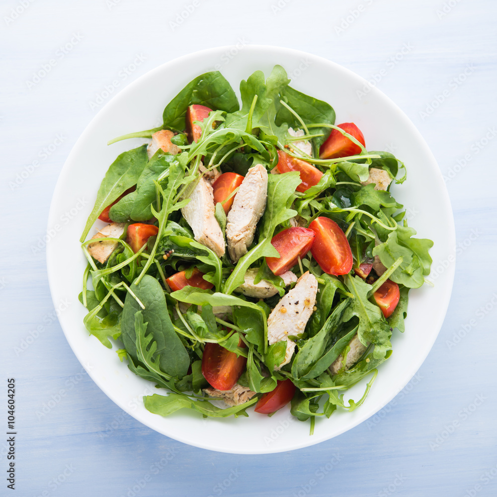 Fresh salad with chicken, tomato and greens (spinach, arugula) on blue wooden background top view. Healthy food.