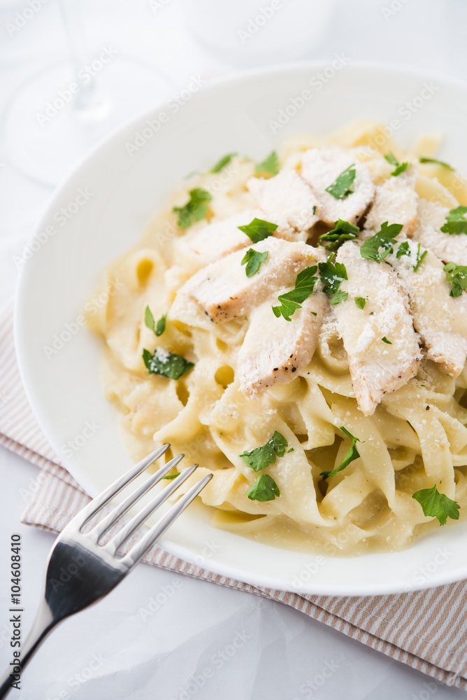 Pasta fettuccine alfredo with chicken, parmesan and parsley on white background close up. Italian cuisine.