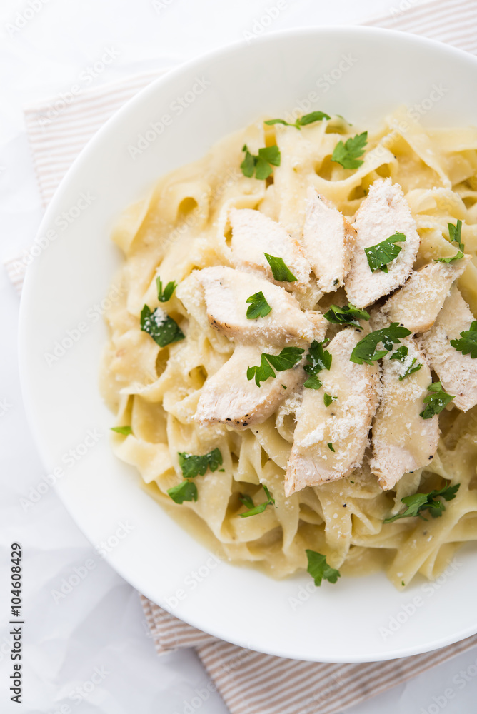 Pasta fettuccine alfredo with chicken, parmesan and parsley on white background top view. Italian cuisine.