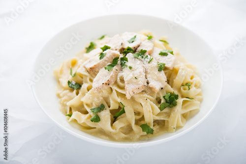 Pasta fettuccine alfredo with chicken, parmesan and parsley on white background close up. Italian cuisine. photo