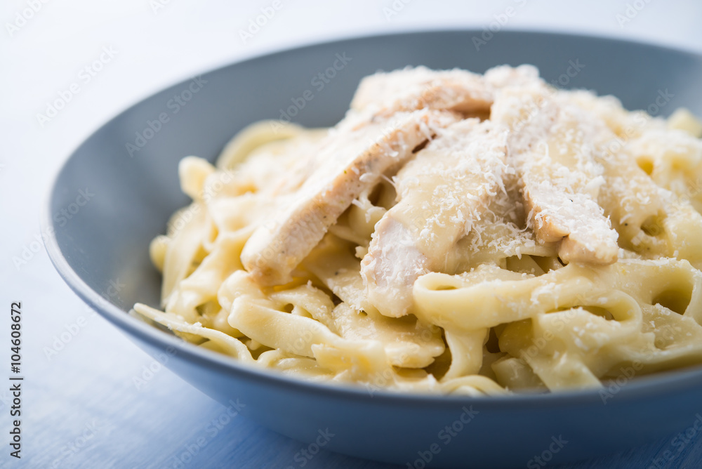 Pasta fettuccine alfredo with chicken and parmesan on blue wooden background close up. Italian cuisine.