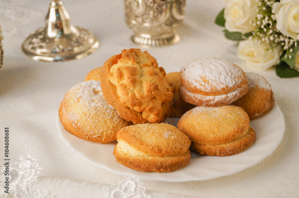 Shortbread cookies sprinkled with powdered sugar on a white plate is on the table, composition, flowers