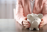 Woman holding in hands piggy bank at the table