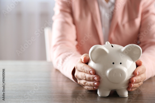 Woman holding in hands piggy bank at the table